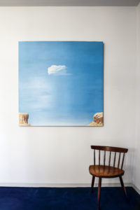 An upstairs vignette with a gifted artwork from Walsh, that originally hung over her fireplace. Woody Gwyn’s metaphoric scene of a floating cloud represents, for the couple, Walsh looking down, while Susan and Raymond are the cliffs. The chair is by Mira Nakashima, daughter of great furniture maker George Nakashima. (Photo by Pär Bengtsson)