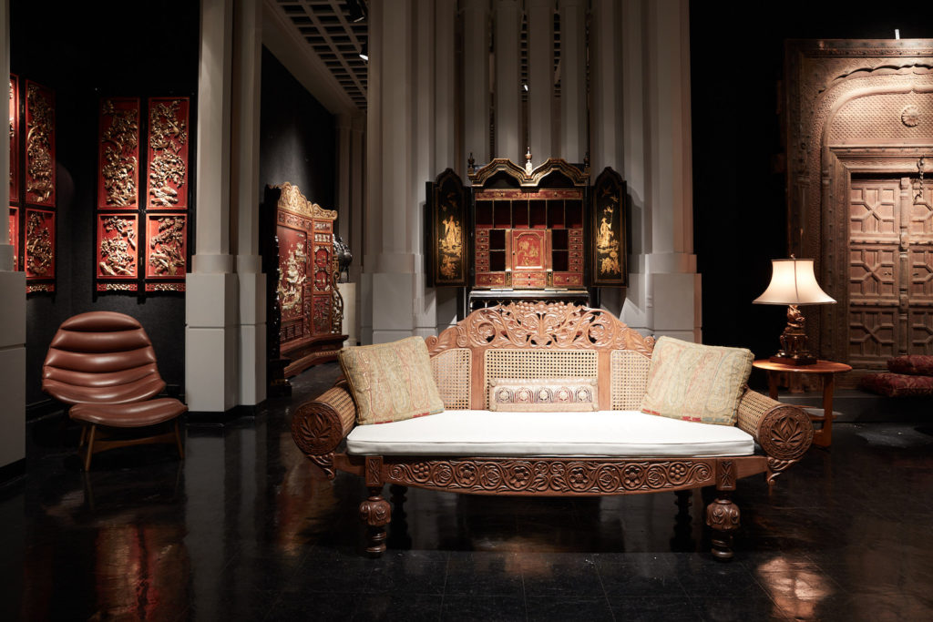 A British Colonial satinwood and cane settee, ornately carved with scrolling foliage, vines, and flowers. An English chinoiserie secretary from the early 20th century has gilt painted scenes of Chinese figures, pagodas, and gardens. (Photo by Pär Bengtsson)