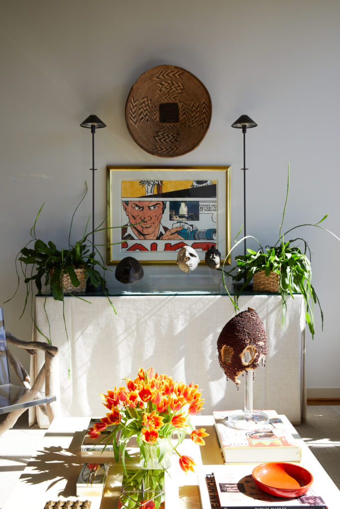 A skirted console in the living room with tribal masks, including one purchased during a trip to Bangkok. Al Souza artwork from Moody Gallery. African basket on wall. (Photo by Pär Bengtsson)