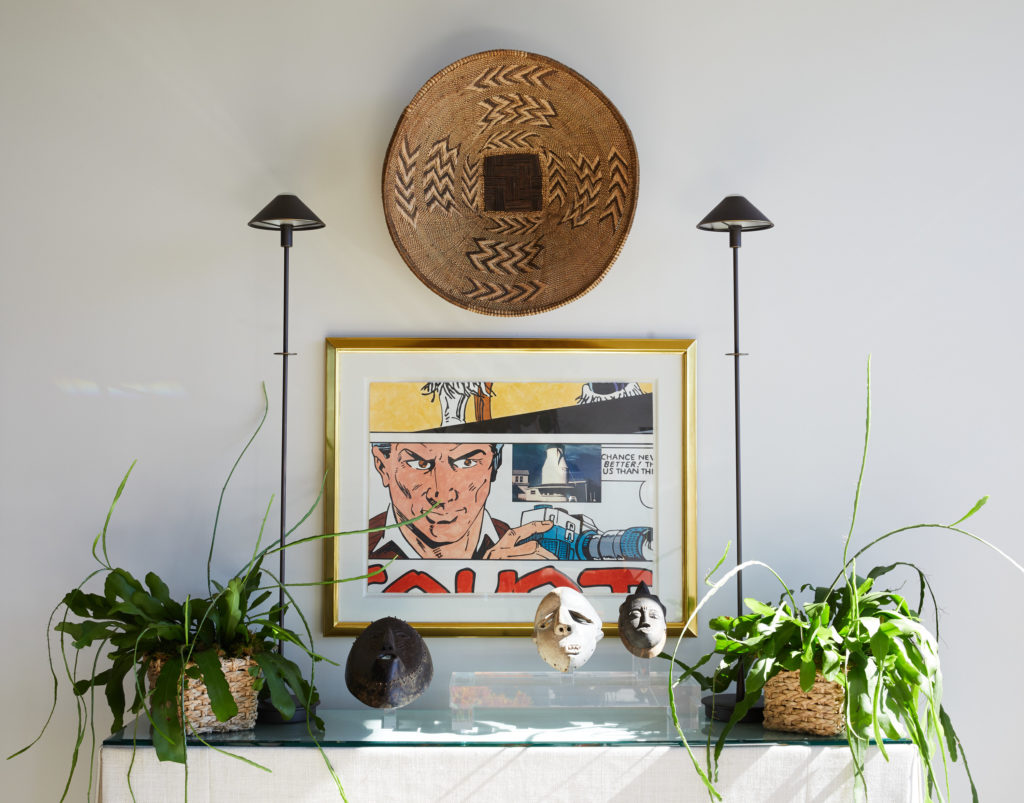 A skirted console in the living room with tribal masks, including one purchased during a trip to Bangkok. Al Souza artwork from Moody Gallery. African basket on wall. (Photo by Pär Bengtsson)