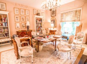 In Betty Gertz’s office, a set of 19th-century chairs, mid-century glass chandelier, English William and Mary chest used for filing, 18th-century botanicals, antique Aubusson rug, and pots and lacquer chests from Burma and Bangkok. Dried vines from the courtyard grow into the room.
