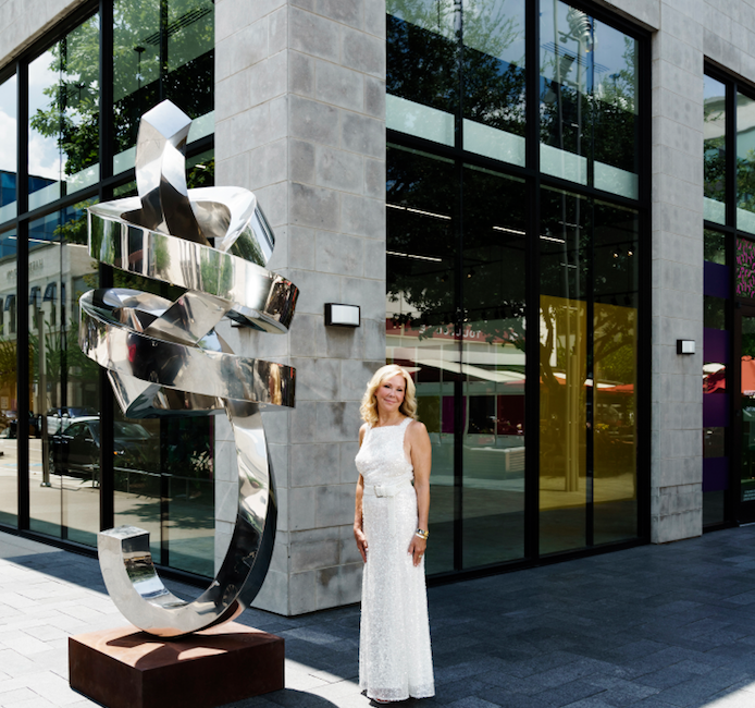 Laura Rathe at the entrance to her new River Oaks District space, unveiling Thursday, October 1. Rathe, who marked her 20th anniversary as a gallerist in 2019, will now have three Texas spaces: her original gallery on Colquitt, a Dallas location in the Design District, and now this high-profile site at River Oaks District. The gallerist stands next to Gino Miles’ stainless-steel sculpture “Omen,” 2019. (Photo by Jack Thompson)