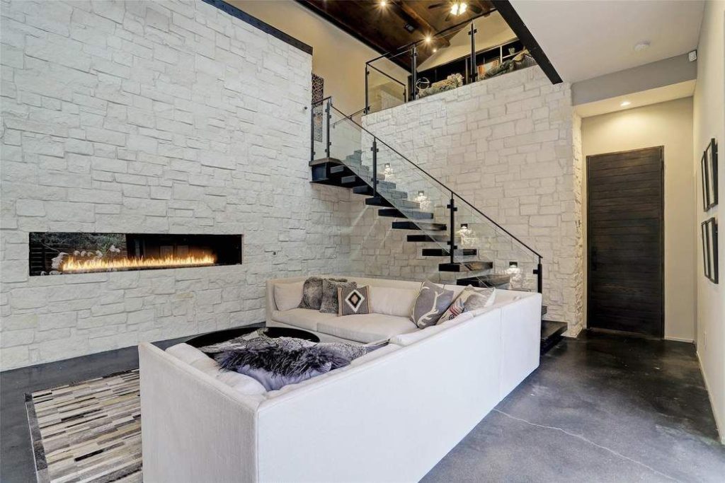 The open living-room floor plan is anchored with a floating stairwell with glass siding and iron railings.