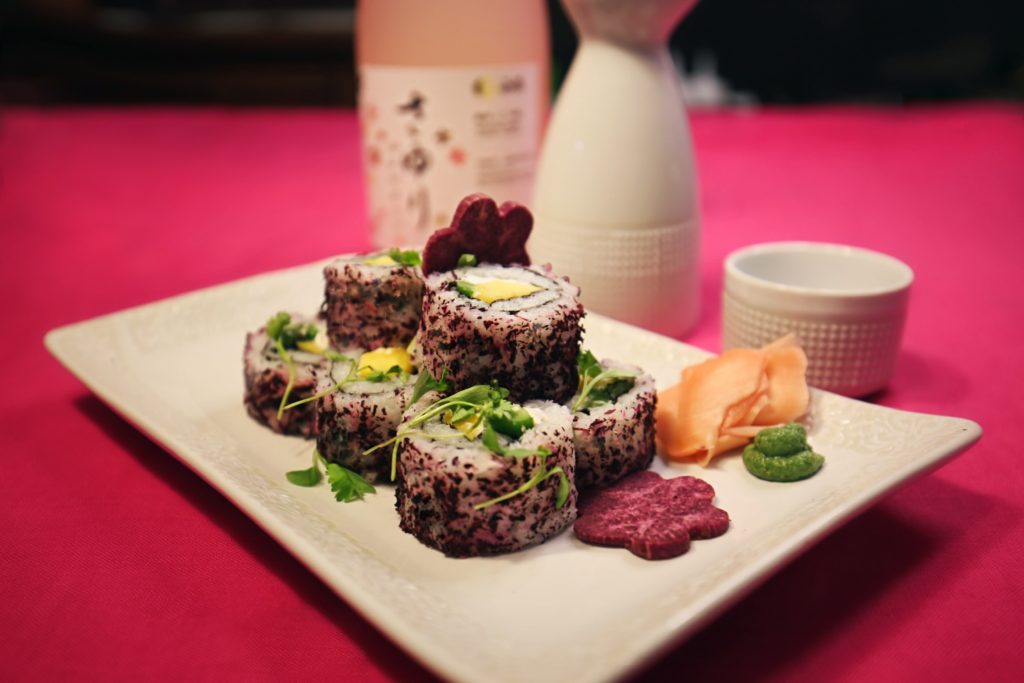 The Healthy and Wealthy Roll is filled with cream cheese, mango, and jalapeño rolled with rice seasoning and micro-greens on a bed of sweet chili sauce.