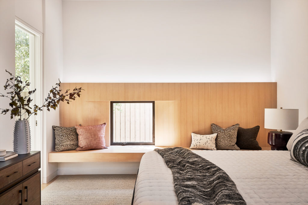Smitharc Architects + Interiors designed a custom white oak wall bench in the main bedroom to complement the house’s other built-in features. A small window overlooks a courtyard. Custom pillows in Duralee fabrics, Uniq’uity throw, Annie Selke bedding, Natan Moss custom lamp. (Photo by Stephen Karlisch)