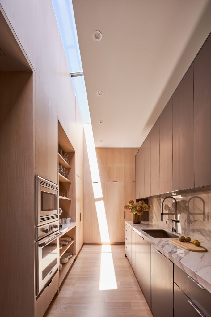 In the prep kitchen, a ribbon of light from the skylight travels like a sundial. White oak cabinets and floors. Sintered-stone countertops. (Photo by Stephen Karlisch)
