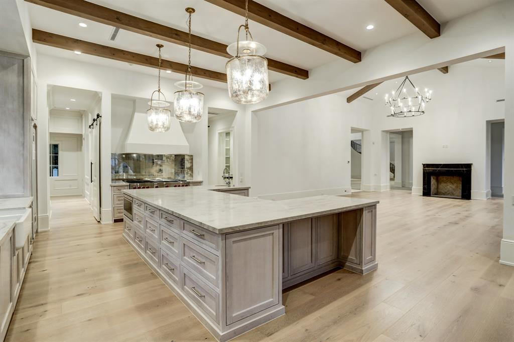 Open kitchen with huge island, slab stone countertops, stainless steel appliances, two sinks, solid stock fir beam ceilings, and white oak floors at 3001 Inwood. (Photo by TK Images)