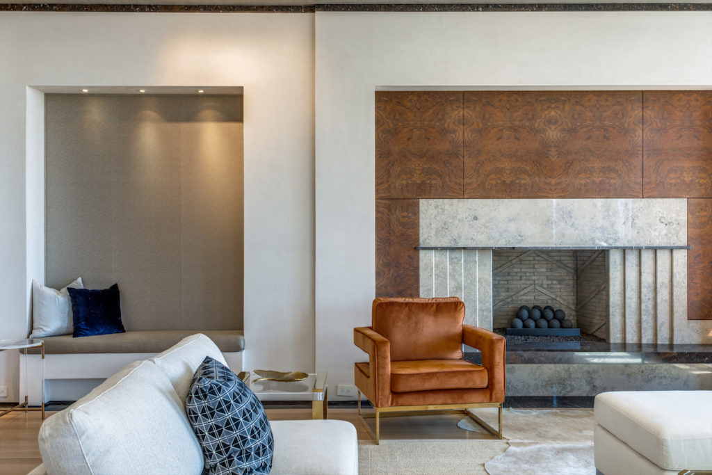 An architectural fireplace and a cozy seating nook bring warmth to the penthouse living room. (Photo by Shoot2Sell for Douglas Elliman)