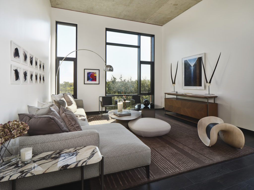 Giorgetti sofa, sideboard, coffee tables and poufs, marble side table, area rug and accent stool.  Poltrona Frau armchairs with wood side table and Flos Floor Lamp.  John David Robbins “Smokes 1-12” series (above sofa), Tyler Shields “RGB” (next to windows) and Caleb Charland “Pouring Light” (above sideboard) artworks. (Photography by Andrea Calo)