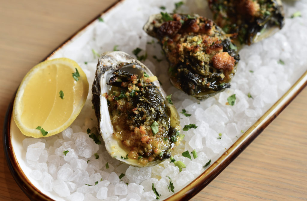 Southern Rockefeller Gulf Coast oysters broiled with old bay-bacon butter, wilted greens, and cornbread crumble. (Photo by Kimberly Park)