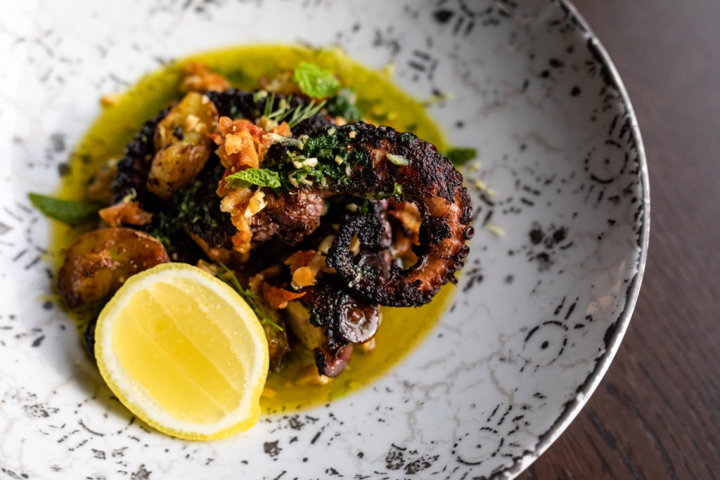 Polpo Arrosto, Wood fire-roasted octopus with Sicilian tomato pesto, crispy potatoes, salsa verde, basil, parsley, and lemon. Photo by Kirsten Gilliam.
