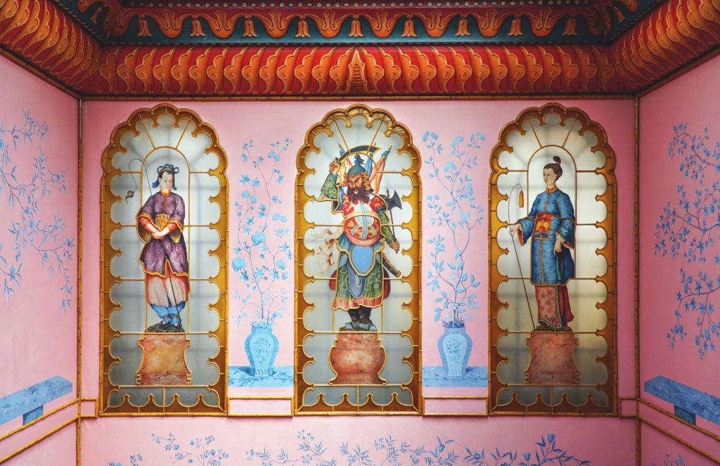 One of a pair of vibrant pink staircases in the Royal Pavilion at Brighton, decorated with blue floral designs and edged with faux bamboo. Beneath a richly painted ceiling, stained-glass windows depict life-size Chinese figures.