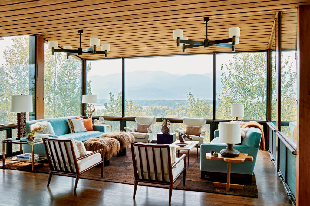 In a house in Jackson Wyoming, the living room is essentially a glass-enclosed tree house that captures exceptional views of the Snake River and the Teton Range in the distance. The chairs in the foreground are vintage T. H. Robsjohn-Gibbings, and the custom area rug is made up of squares of sheared fur.