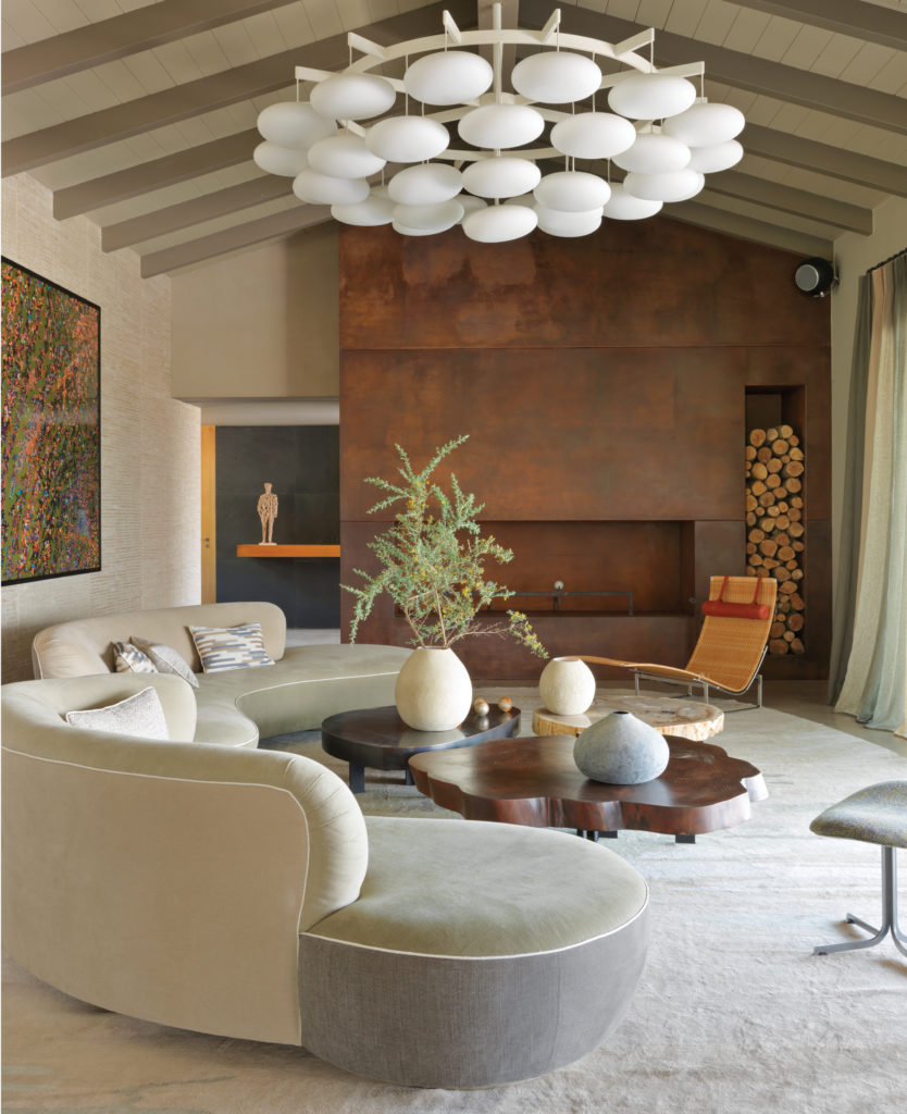 In a villa near Porto-Vecchio in Corsica, Jean-Louis Deniot was inspired by the local landscape. Living room with curved vintage Vladimir Kagan sofas in Romo linen and cotton; set of custom-designed tables in petrified wood, stained sequoia, and bronze; 1950s chandelier by Oswald Haerdtl. (Photo by Stephan Julliard)