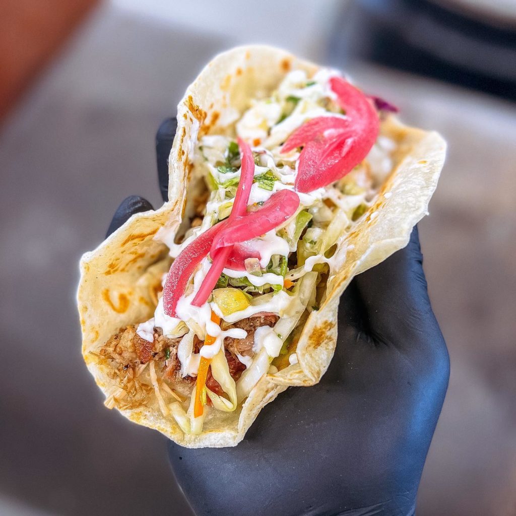 The pulled pork taco topped with pineapple slaw, cilantro lime vin, crema and pickled onion.