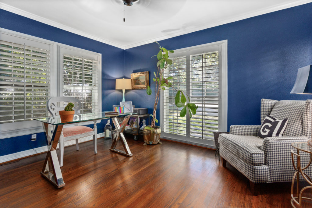 Office setting with plantation shutters, warm wood flooring and energetic blue wall paint.