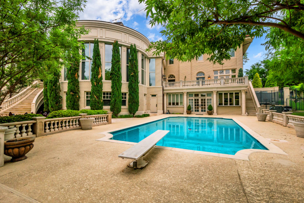 The expansive back elevation includes a modern outdoor kitchen, along with inground pool and stately gardens.