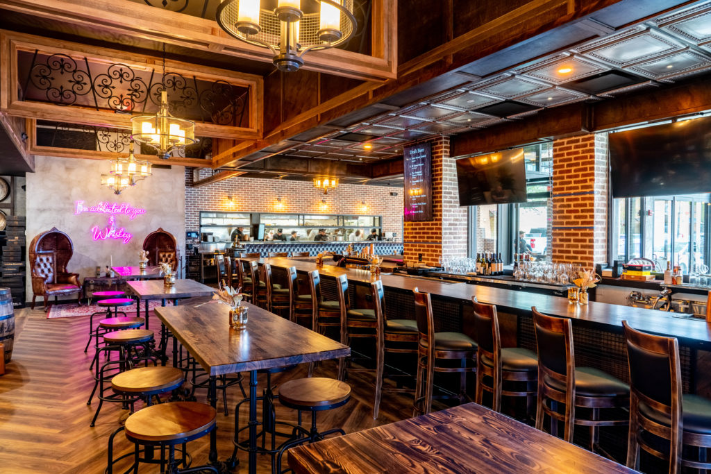 Inside the new Bosscat, the 5,000 square foot space with seating for 130 guests plays off the trend of industrial, rustic aesthetics–read: exposed brick, reclaimed wood, dark leather banquettes, and massive whiskey barrels all over the place. (Photo by Dylan McEwan)