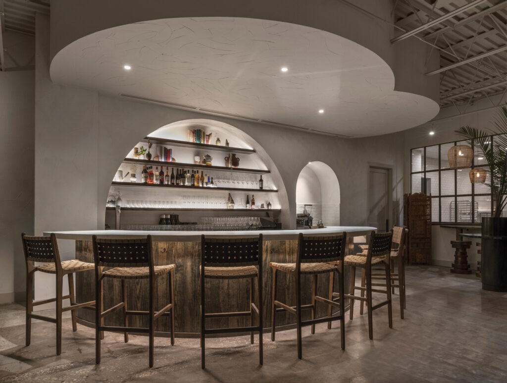 Taking center stage, the massive half-moon shaped bar features a warm white concrete top and illuminated asymmetrical arched shelving. (Photo by Claudia Casbarian with JIA Media)