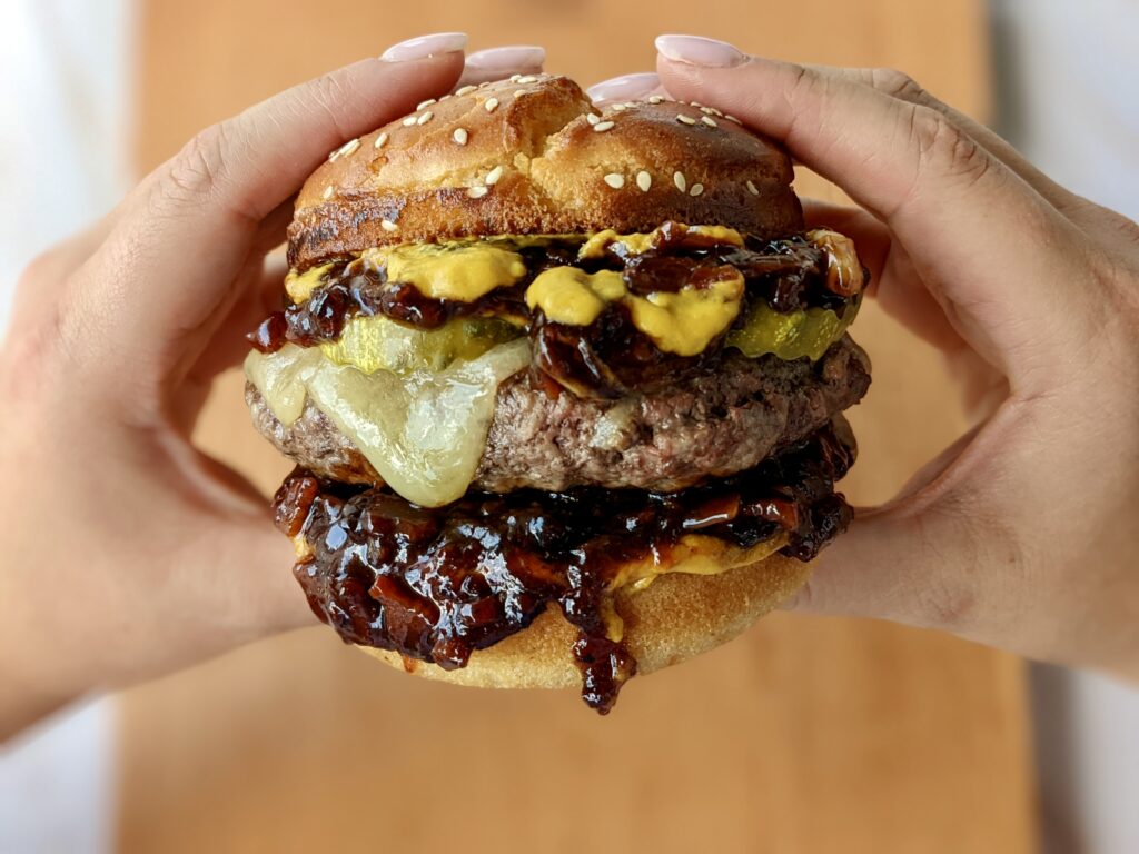 Picnik's mighty grass-fed burger ($20) is sure to quell the fiercest appetite. Topped with melting organic raw cheddar house-made bacon jam and pickles it is sandwiched between a scratch-made sesame bun. (Photo by Kimberly Davis Photography)