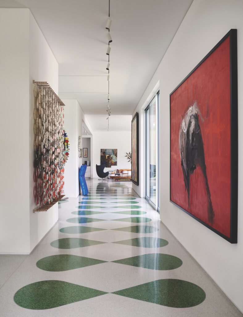 The front hallway’s custom terrazzo floors, laid by National Terrazzo Tile & Marble, were inspired by the Havana Riviera in Cuba. Right, red painting by Tonio Trzebinski. Left, Jacob Hashimoto’s kites. Metal pool float sculpture by Will Cannings. Vintage egg chair. Painting by Inga Kimberly Brown. Small orange boot lithograph by Andy Warhol. (Photo by Pär Bengtsson)