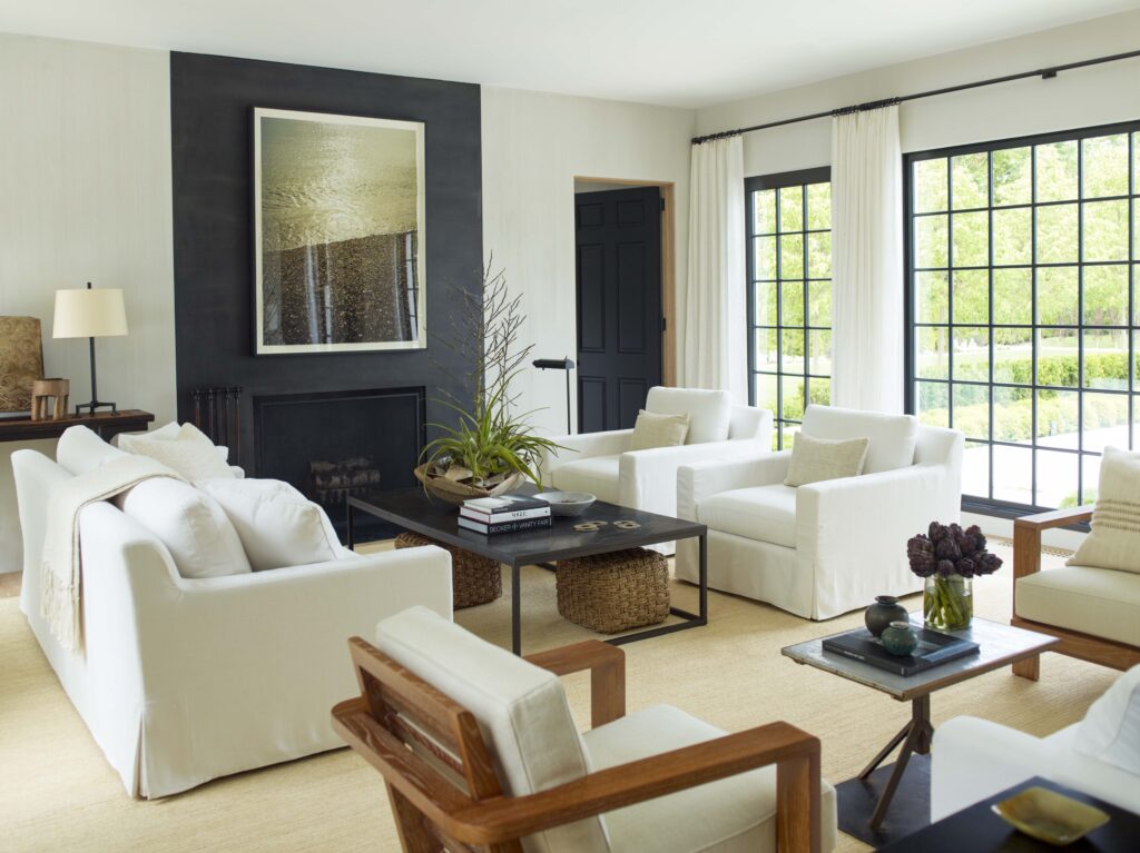 A living room designed by Sawyer | Berson features a blackened-steel fireplace and chimney breast with a photograph by Jack Pierson. Linen-slipcovered upholstery is grouped with a hemp rug and steel-and-wood occasional pieces. (Photo by Eric Piasecki)