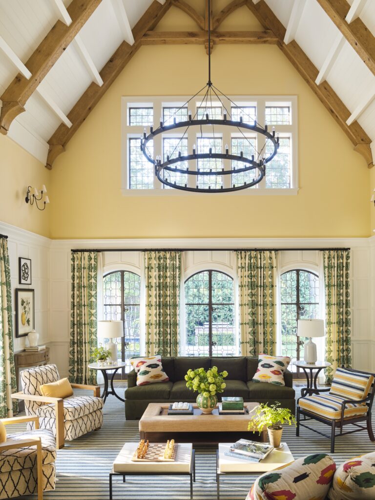 The double-height family room, designed by Carrier and Company, unfolds off the kitchen and is the space where everyone gathers. The panel detail replicates the original elsewhere; painted white, and combined with the vibrant yellow walls above, it makes the room glow. (Photo by Annie Schlechter)