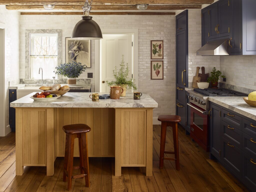 In the kitchen, new glossy variegated-white tile on the walls and marble countertops join the salvaged wood beams of the ceiling and historic floor planks, in a house designed by Peter Pennoyer. (Photo by Eric Piasecki)