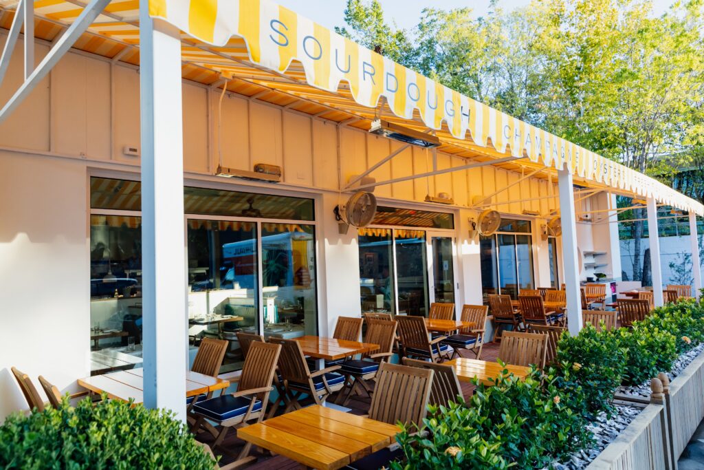 Beneath the marigold yellow-and-white awning in the expansive outdoor space, crowds looking to see and be seen are seated on cushioned deck chairs like you might find on the QE2. (Photo by Justin Book)