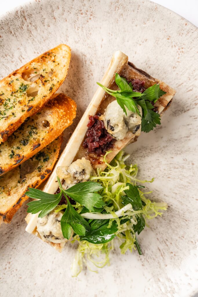 The roasted bone marrow at Annabelle Brasserie is topped with shallot bacon jam, tempura-fried escargot and spears of grilled bread ($28). (Photo by Brian Kennedy)