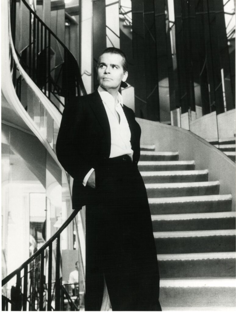 January 1983, Karl Lagerfeld is named artistic director of Chanel, and is immortalized by Helmut Newton on the mirrored staircase at 31, rue Cambon where Gabrielle Chanel once perched. (Courtesy Patrimoine de CHANEL, Paris; © The Helmut Newton Foundation)