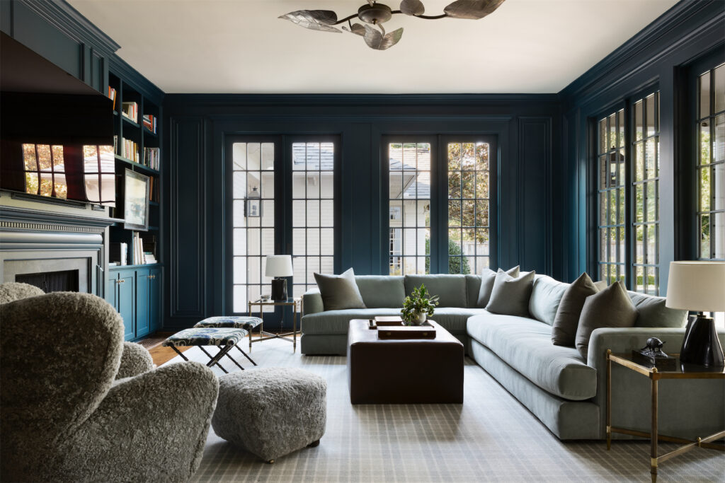 The family room is painted Farrow & Ball Hague Blue. Brass 1970s ceiling lamp from 1stdibs. Maiden Home sectional. Maison Jansen brass side tables. Audo sheepskin lounge chair and footstool from Copenhagen. Vintage 1960s brass benches from 1stdibs. Kim Salmela custom ottoman. Elan Atelier lamps from David Sutherland Showroom. Stark rug. (Photo by Trevor Parker)