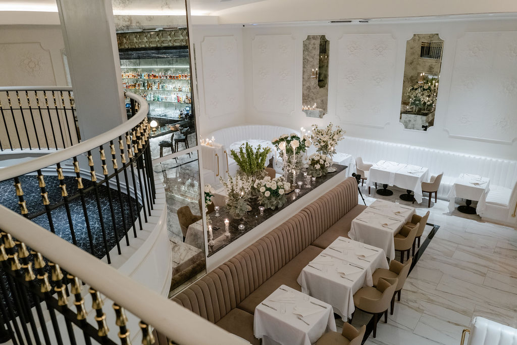 Inside the main dining room, white plaster-adorned walls and pearlized white leather channeled banquettes are punctuated with rich, dark hues. The room, expansive in both height and length, is magnified further by antiqued mirrors, while upstairs, dinner is served to the accompaniment of a baby grand piano. (Photo by Brian Kennedy)