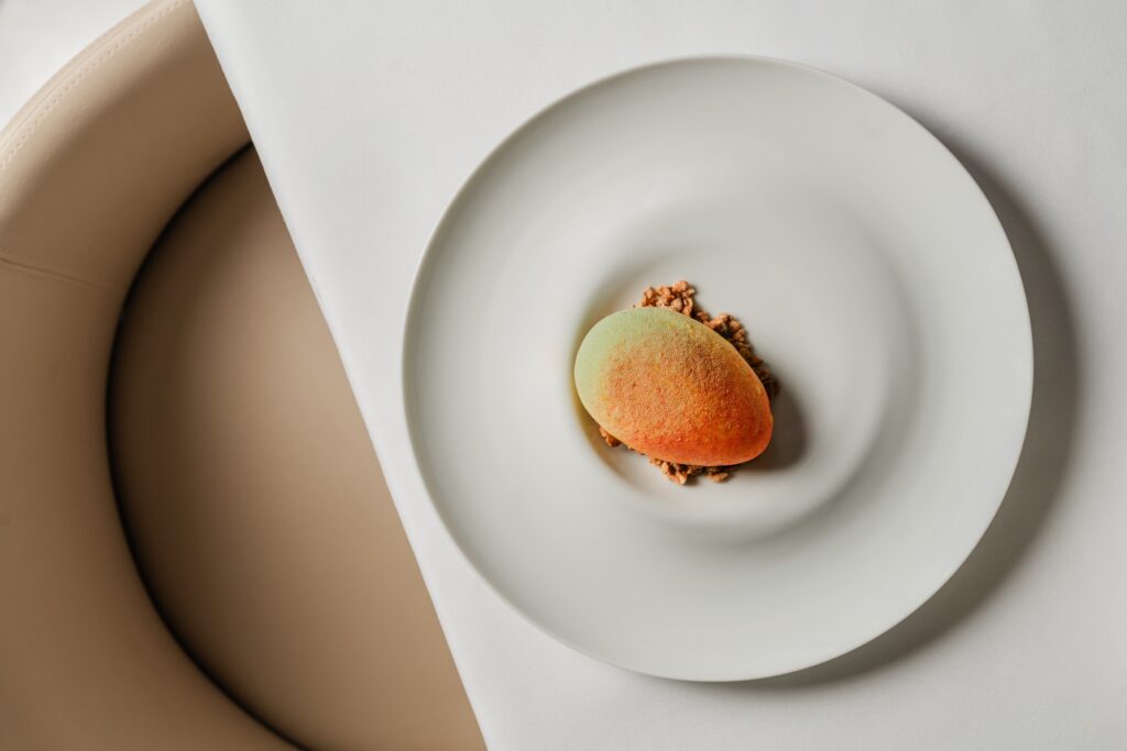 Playing with the concept of trompe l’oeil, the "mango" looks like the tropical fruit but is actually a white chocolate shell painted like the exterior of a sweet Alphonso mango, filled with mango mousse, atop a bed of crispy hazelnut crumble ($17). (Photo by Brian Kennedy)