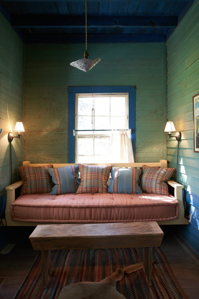 The house was built in 1890 as a stagecoach stop that included this Stranger's Room for weary travelers. The floor is not level so Bill Curtis designing a hanging daybed. Walls are washed with green stain, and press tin covers a hanging bulb. Antique bench and hooked rug. (Photography Pär Bengtsson)