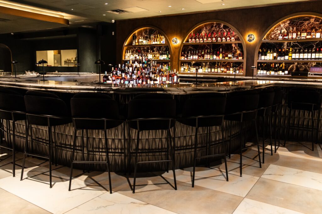 The moody-lit dining room and adjoining bar at Okto are awash in emerald tones with glints of golden brass and solid marble accents created by interior designer Lindsay Madrigal of LM Designs. (Photo by Becca Wright)