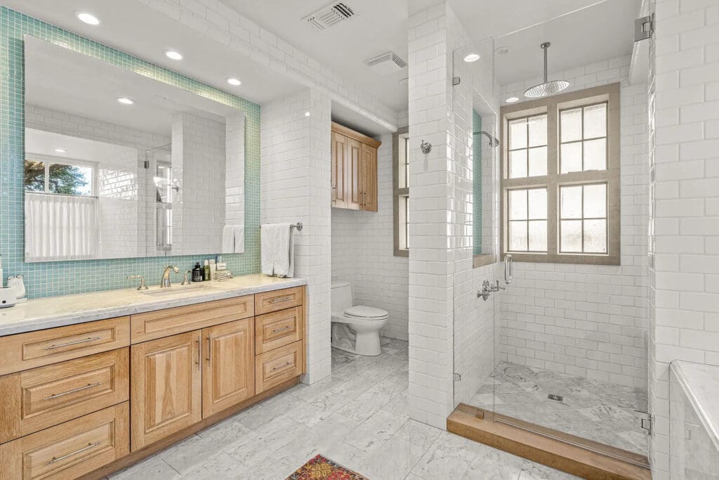 6308 Indian Creek Drive's primary suite's en-suite bath features marble flooring, a glass-enclosed shower, and custom wood cabinetry. (Courtesy)