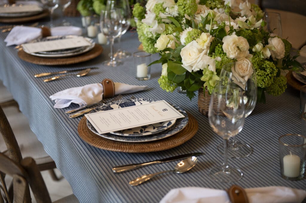 A classic tablescape (e.g. a striped tablecloth, leather napkin rings, rattan chargers, and blue and white china) accompanied the distinctly American meal. (Photo by Tamytha Cameron)