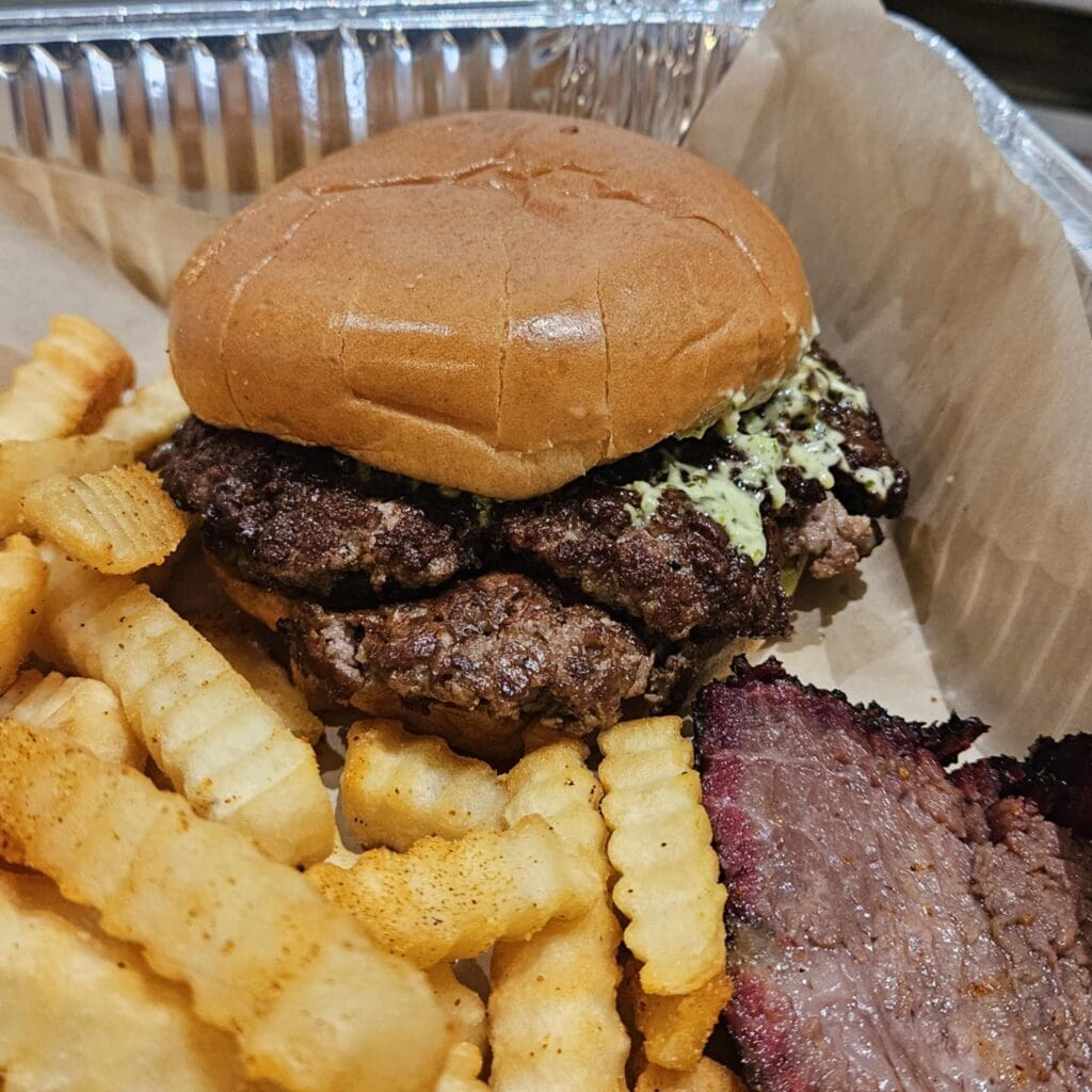 The Le Brix Burger stacks two seared brisket patties with cheddar, pickles, onions, and a slather of creamy “dank sauce.” (Photo by Edward Brown)