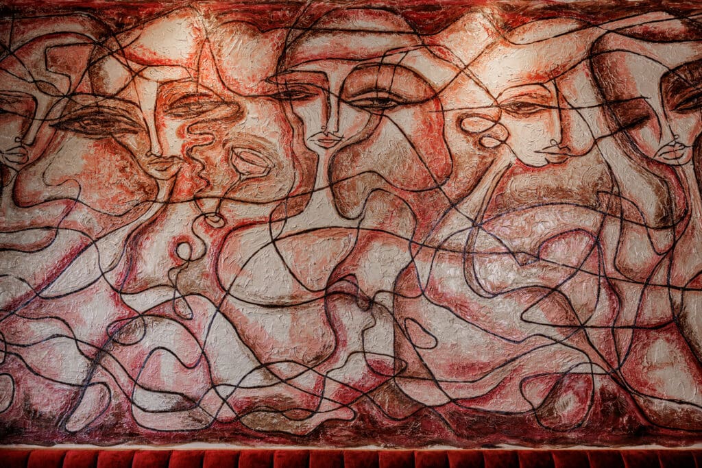 The interior boasts lots of pinks, velvet banquettes, an open kitchen, a large red stone bar top, and a 315-square-foot mural inspired by Picasso by local artist Jennifer Kindert. (Photo by Samantha Marie)