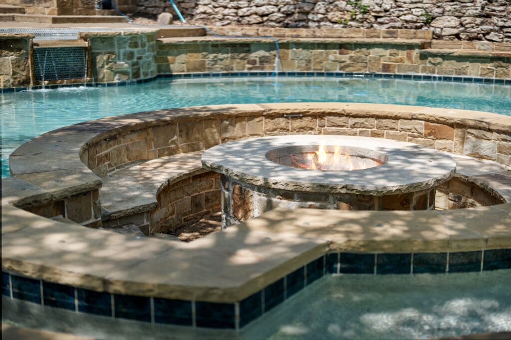A sunken fire pit is carved directly into the stonework beside the pool — perfect for evening gatherings under the stars.  (Photo by The Ashton Agency)