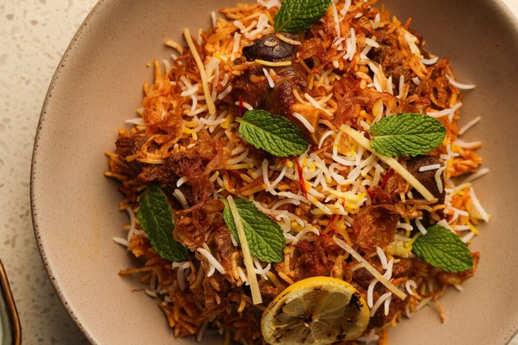 The goat biryani ($26) at Kitchen Rumors sees small chunks of bone-in goat meat are scattered through the aged basmati rice, topped with dried slivered onions, and by its side, a cool yogurt sauce. (Photo by Chris Furia)