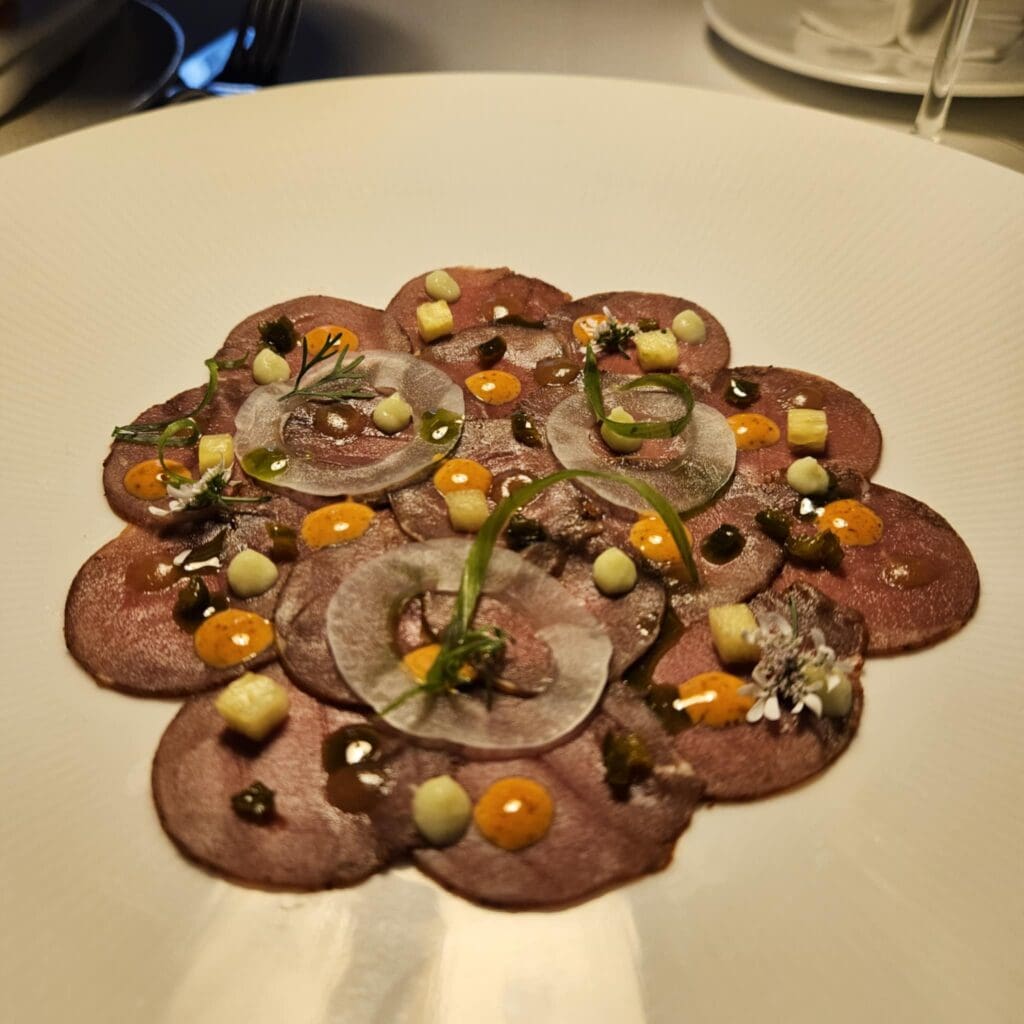 Venison carpaccio “al pastor” at The Crescent Hotel’s Blue Room is sliced thin and topped with fermented pineapple, house-made gochujang, candied serrano, and cilantro blossom. (Photo by Edward Brown)

