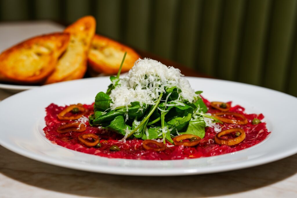 Texas Black Angus carpaccio ($18) topped with a tangle of arugula leaves, fried capers, and pickled shallots with crisp crostini. (Photo by Michael Ma)