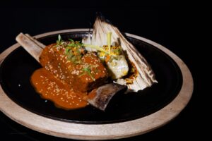 14. Braised Beef Rib a La Mexicana is a slow-braised beef rib with corn tamal, pipián rojo, and nopales escabeche.