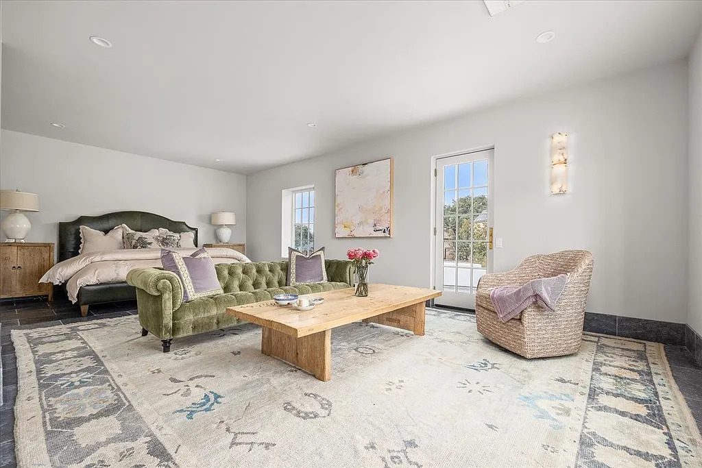 The expansive primary suite balances comfort and scale, featuring a sitting area, soft neutral tones, and garden-facing French doors. (Courtesy)