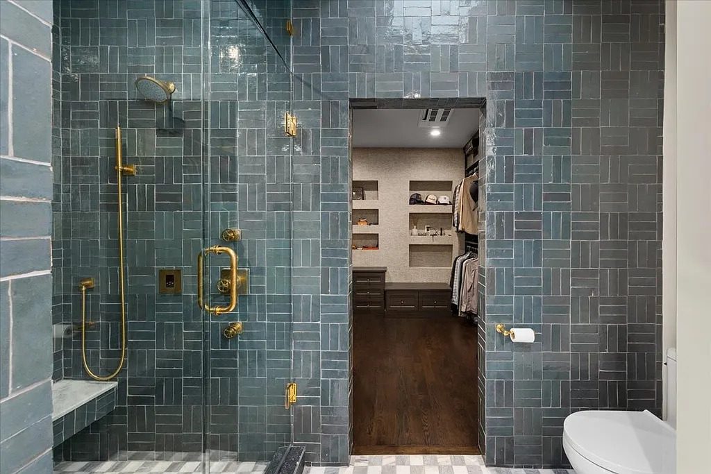 A richly tiled primary bath pairs deep blue-green stone with polished brass fixtures, opening directly into a custom walk-in closet. (Courtesy)