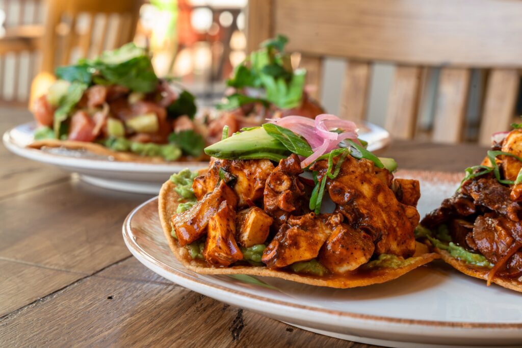 An array of tostadas includes the El Brazo ($22), featuring octopus mingled with redfish in a Roja salsa marinade, topped with sliced avocado and a sprinkle of Tajin. (Photo by Hasan Yousef)
