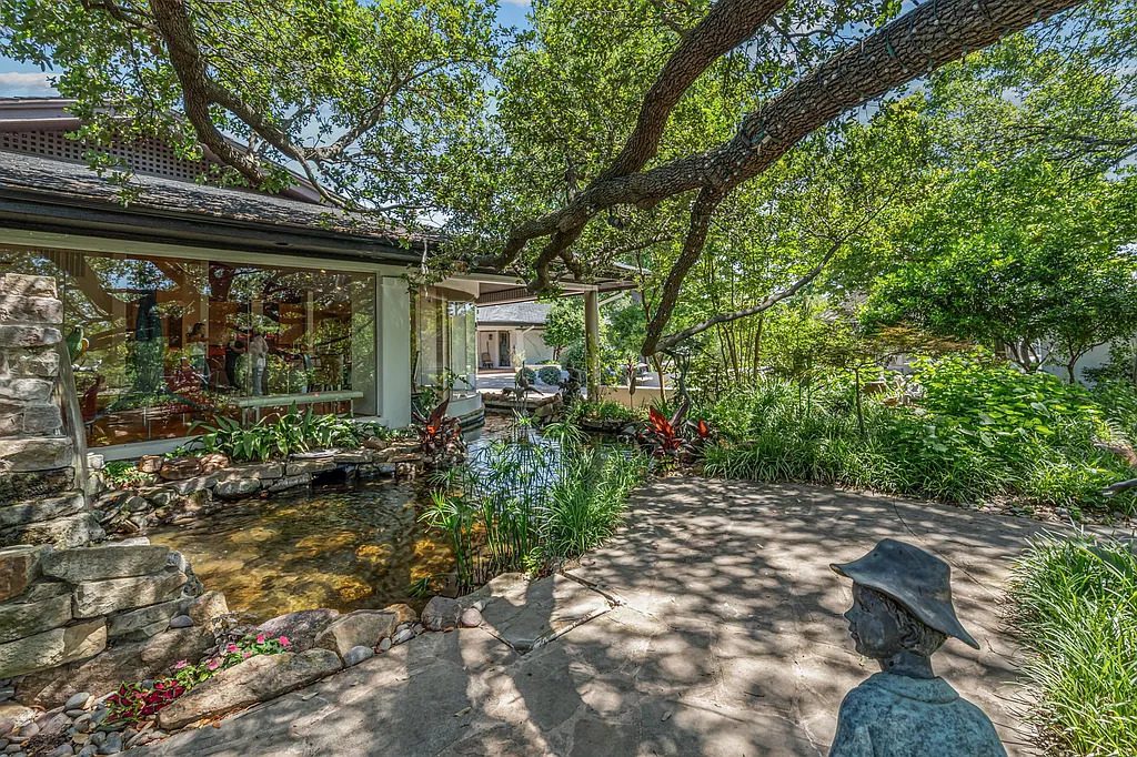 A shaded patio wraps around one of the koi ponds at 4301 Briarhaven Road, where layered stonework, lush plantings, and overhanging tree branches create a quiet, garden-like setting. (Courtesy)