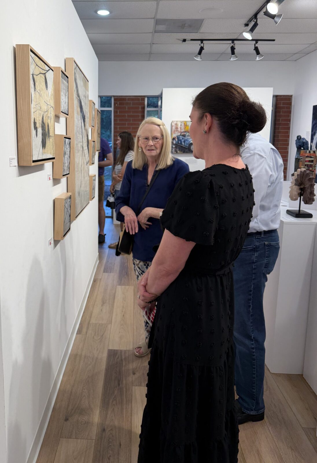 Gallery owner Julie Verville and gallery guests with the encaustic wax pieces of "The Mending Project."  (Photo by Laura Landsbaum)